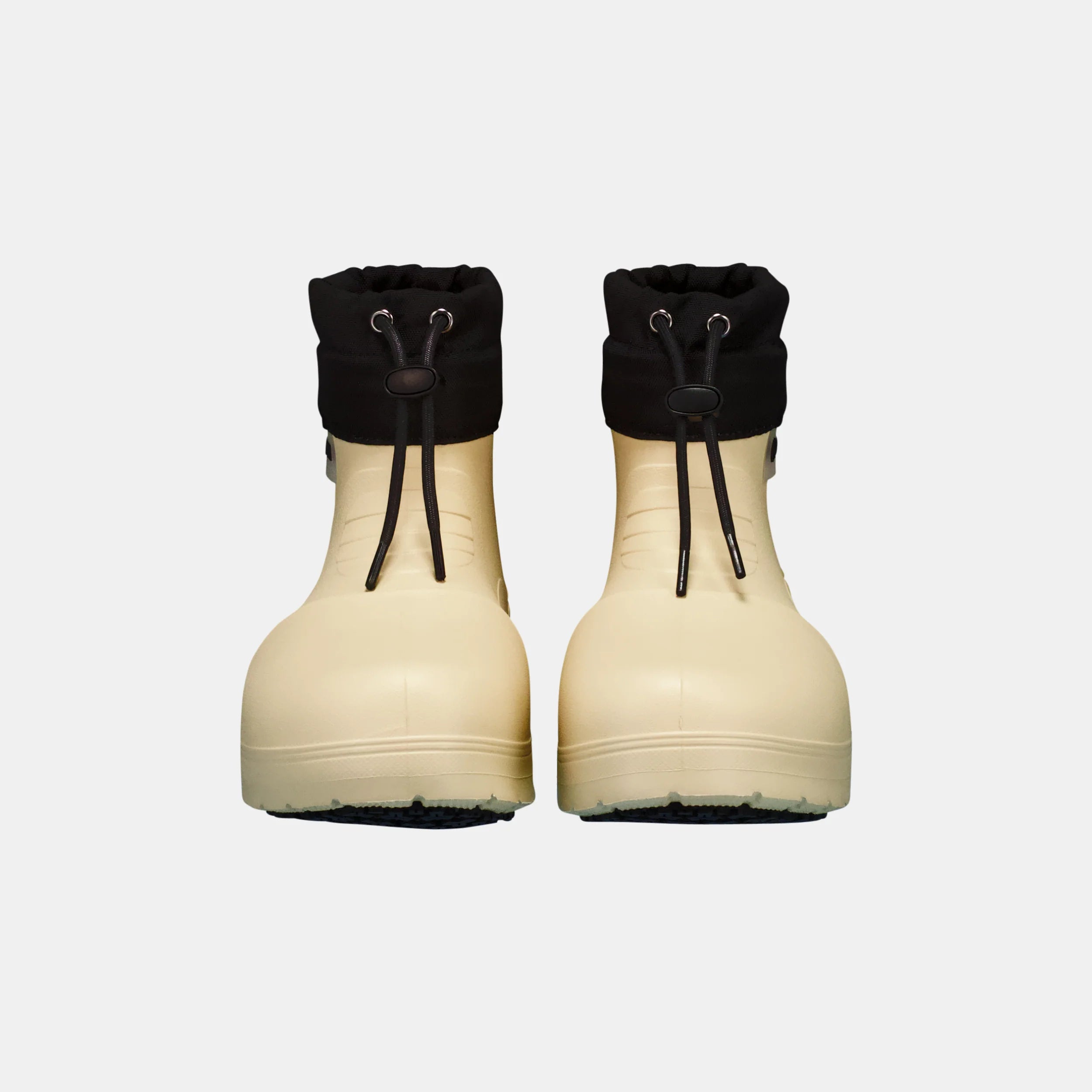 Pair of beige rubber boots with black cuffed tops on a white background