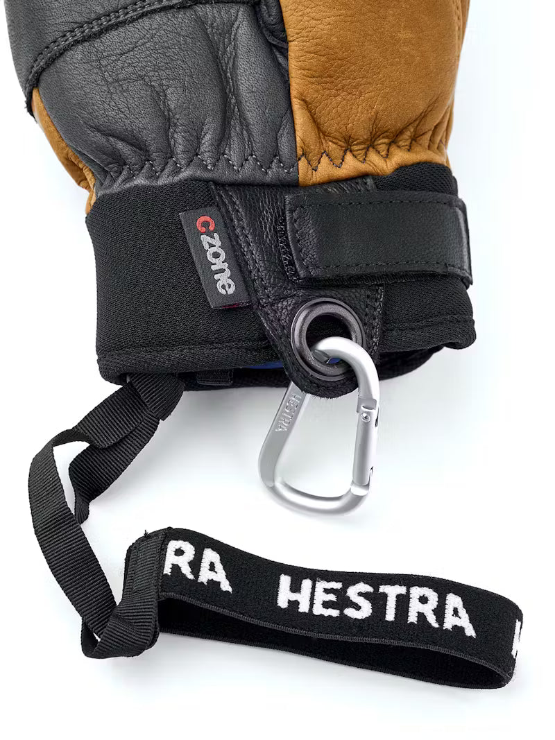 Close-up of a glove with a carabiner and lanyard, featuring Hestra branding.