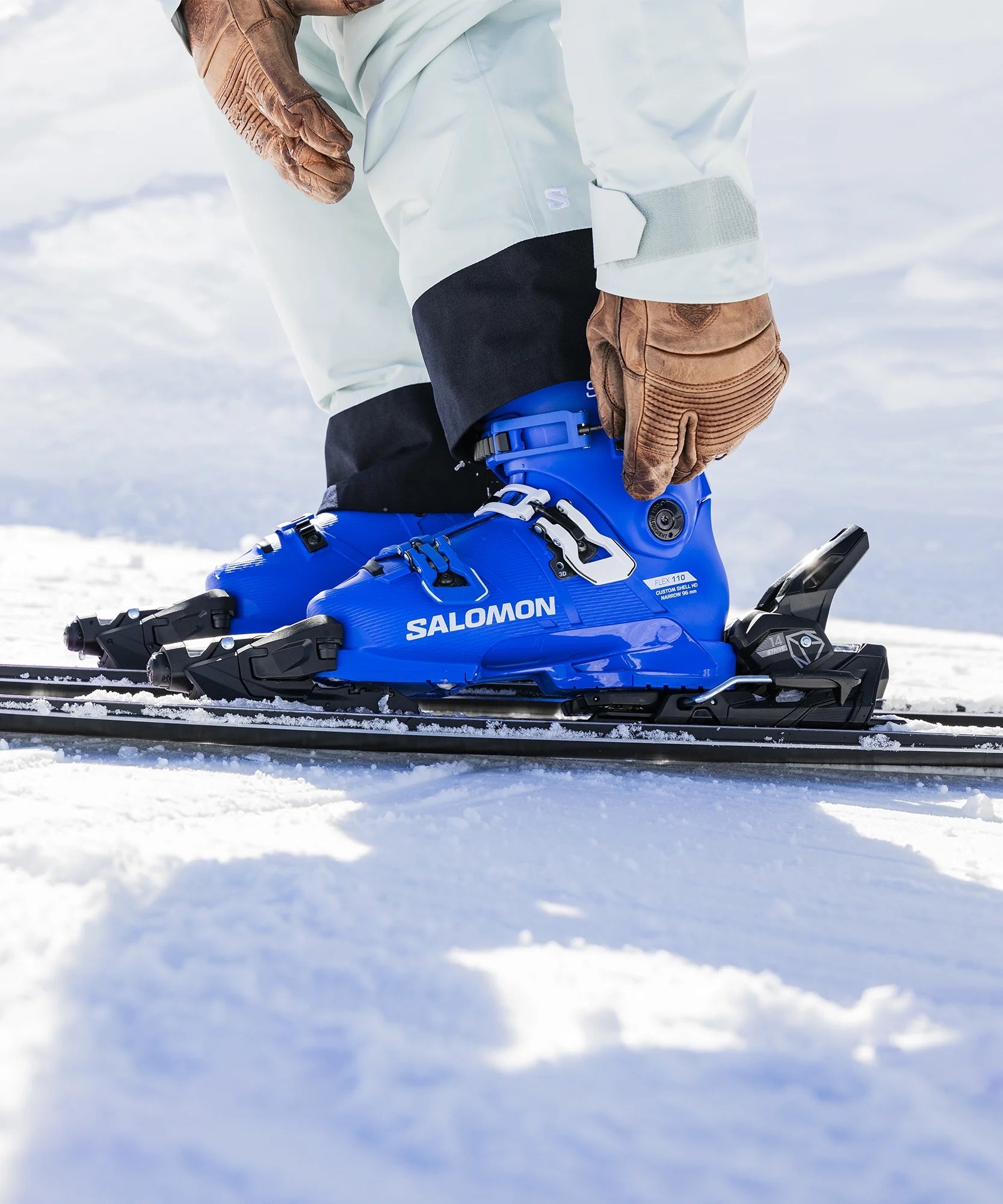 Blue Salomon ski boot being worn on a snowy surface stapped into ski bindings.