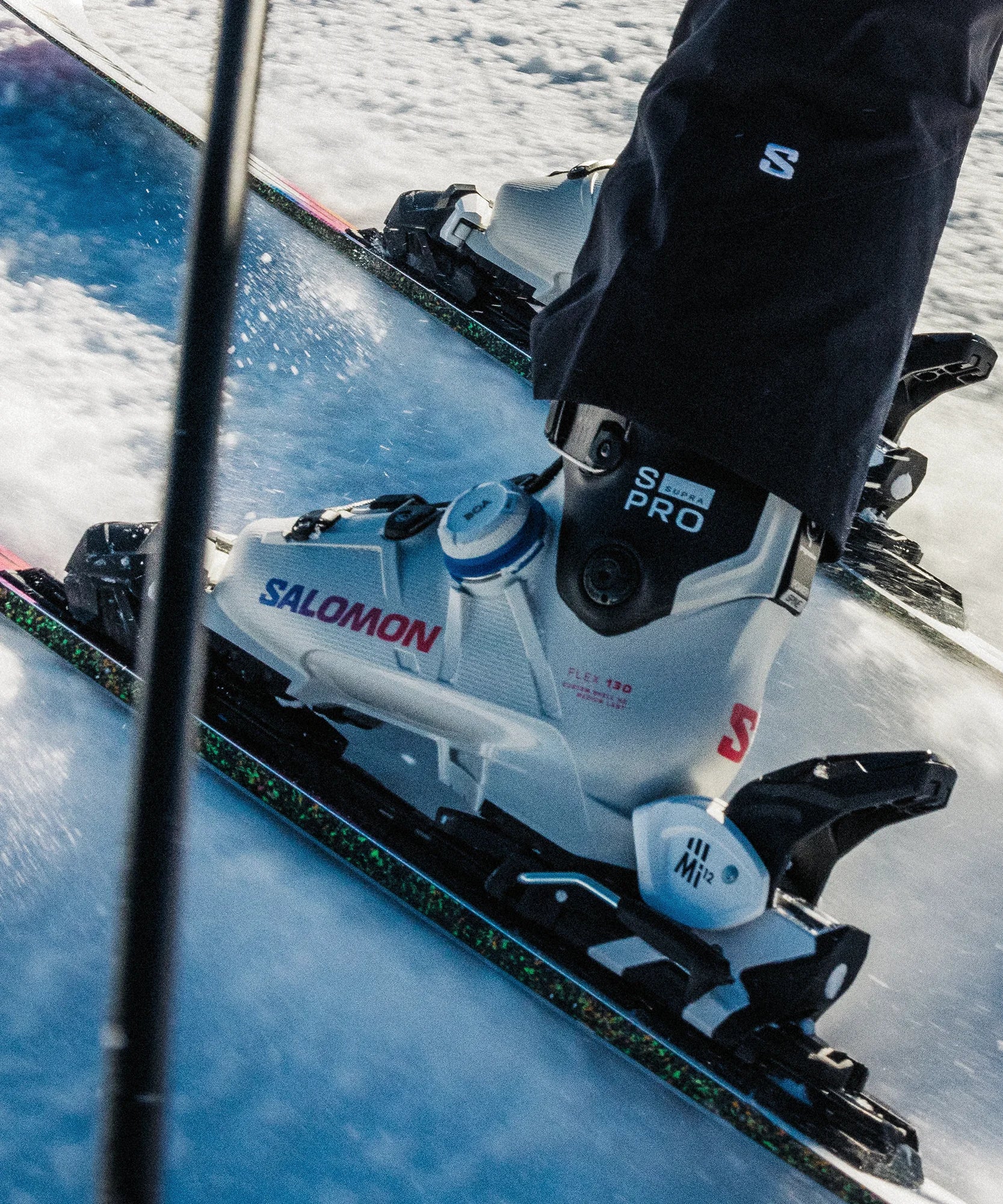 Close-up of a ski with Salomon ski boots clicked into Salomon bindings on a snowy surface.